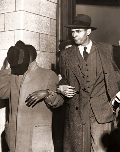 窃盗犯と手錠でつながれて、ニューヨークの連邦裁判所を出るアルジャー・ヒス かつて共産党員だったことを否認したため、偽証罪に問われ5年の刑を宣告された [ジャック・バーンズ, 1951年, 栄光の「LIFE」展 1946-1955 時代の顔を衝くより] パブリックドメイン画像 
