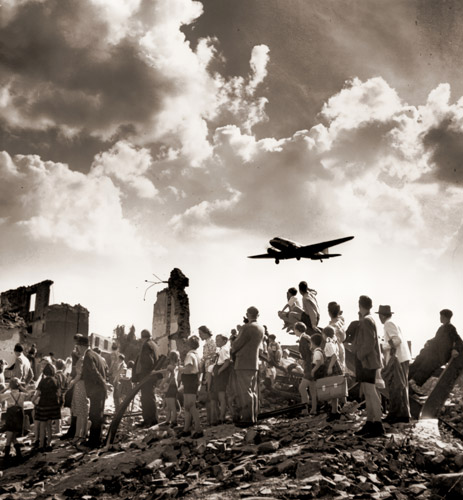 ソ連のベルリン封鎖に対し西側が行なった空輸作戦のさなか、テンペルホフ飛行場の廃嘘から食料補給のC-47機を見上げる市民たち [ウォルター・サンダース, 1948年, 栄光の「LIFE」展 1946-1955 時代の顔を衝くより] パブリックドメイン画像 