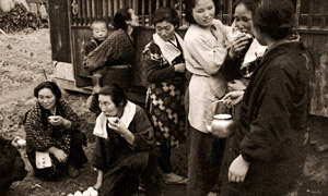 祖母と嫁ぐ孫娘(招かれない嫁見の村人たちにも外で白い酒がふるまわれる） [岩田幸助, 日本カメラ 1956年1月号より]のサムネイル画像